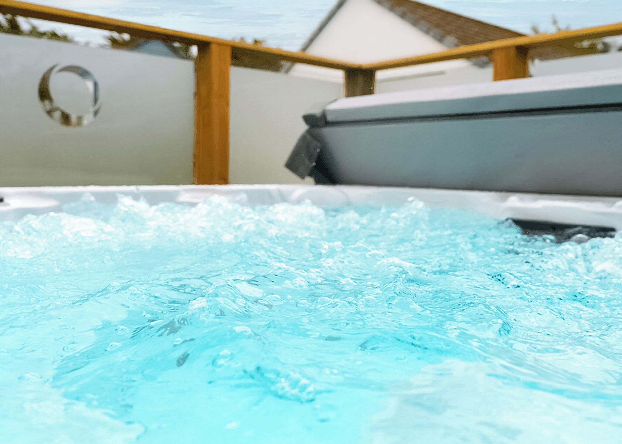 A hot tub with water bubbling, surrounded by wooden beams and a white wall.