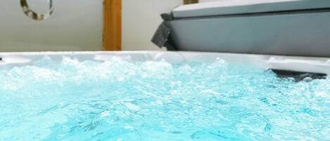 A hot tub with water bubbling, surrounded by wooden beams and a white wall.