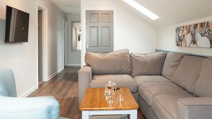 A modern living room with a sectional sofa, a wooden coffee table, and a flat-screen TV mounted on the wall. - Ocean Tide Villa 3 Hot Tub (Woolacombe)