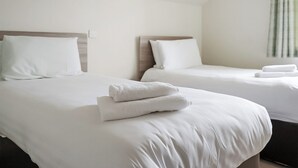 Two single beds with white linens, a wooden headboard, and a neatly folded towel on the bed. - Ocean Tide Villa 3 Hot Tub (Woolacombe)