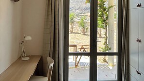 A room with a desk, chair, and a view through a glass door to an outdoor area with a table and chairs. - Queen Deluxe Studio (Favignana)