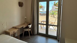 A bedroom with a bed, a desk, and a chair. There is a window with a view of a beach and a building. - Queen Deluxe Studio (Favignana)
