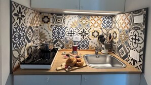 A kitchen with a patterned backsplash, a sink, and a countertop with a cutting board and bread. - Queen Deluxe Studio (Favignana)