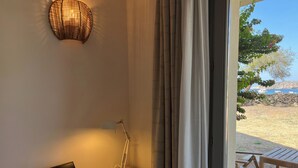 A laptop on a desk with a lamp, a glass of water, and a view of the outdoors through a window with curtains. - Queen Deluxe Studio (Favignana)
