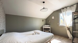 A bedroom with a bed, a bedside table, a hanging light fixture, a window with curtains, and a view of the outdoors.