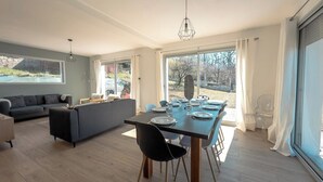A spacious living area with a dining table, sofa, and large windows.