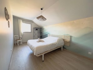 A bedroom with a bed, a chair, a window, and a wall-mounted radiator.