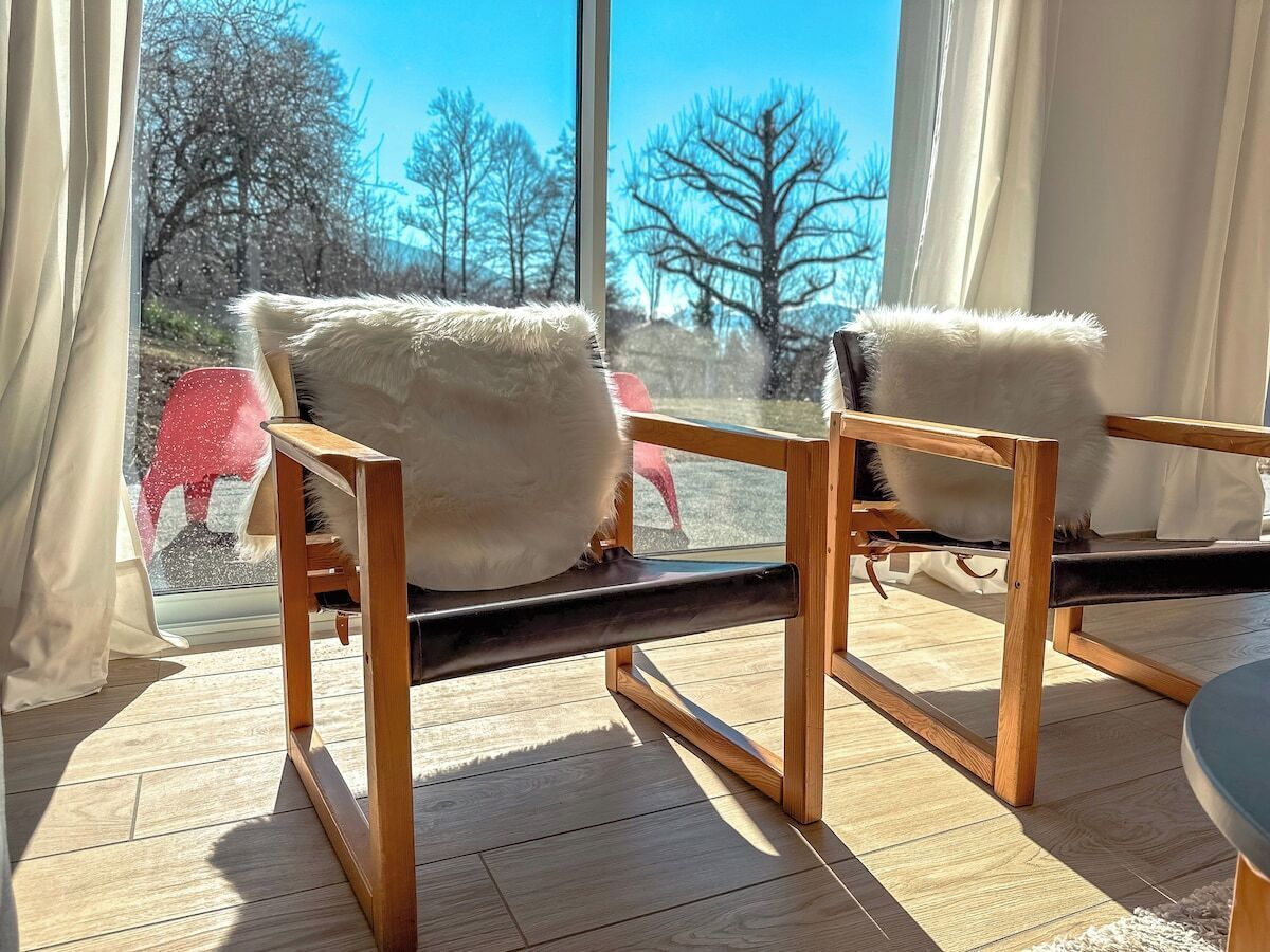 Une chaise en bois avec des coussins blancs, dans une pièce dotée de grandes fenêtres.