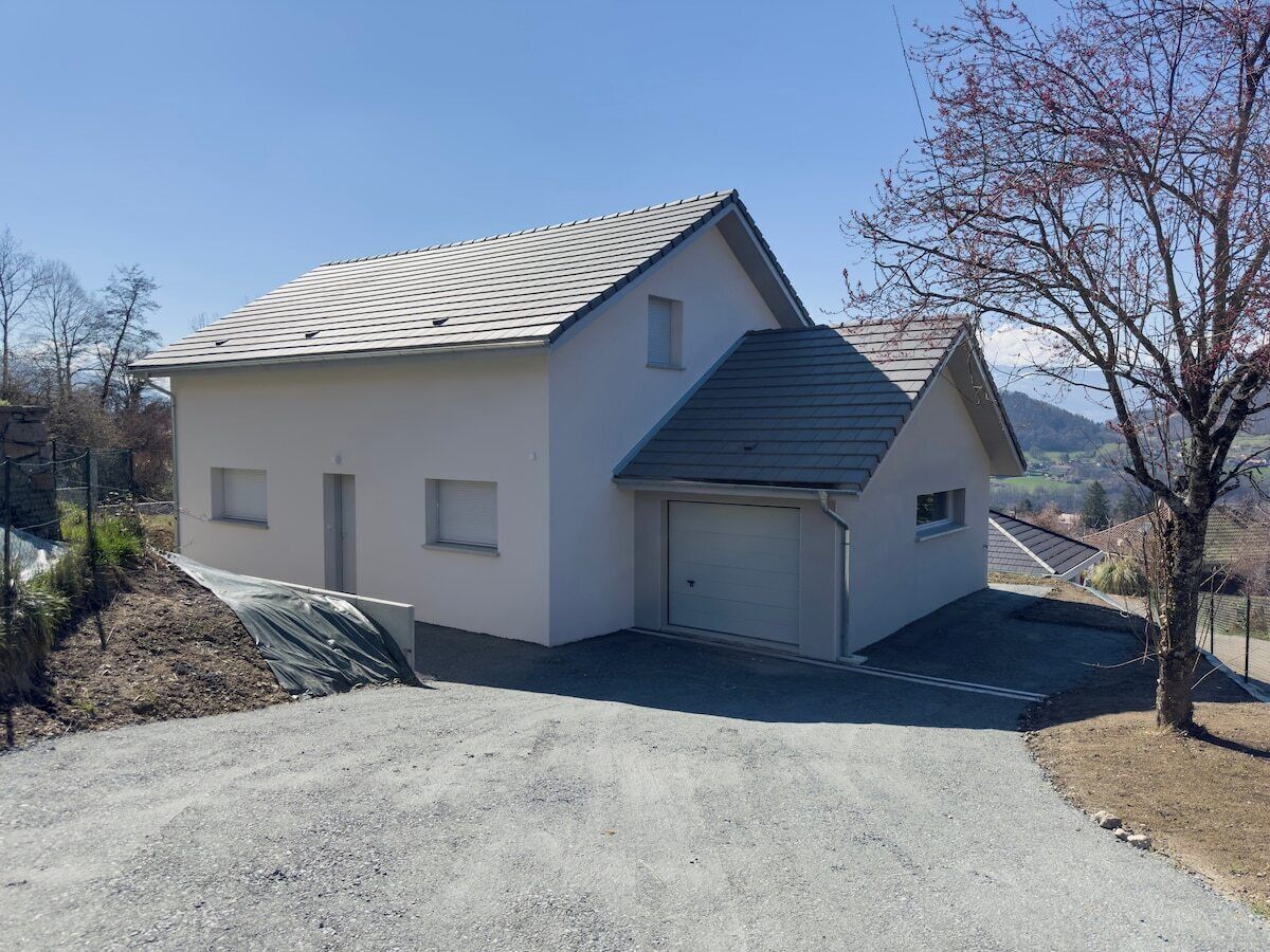 Une maison de plain-pied avec un garage, un toit en pente et une allée gravillonnée.