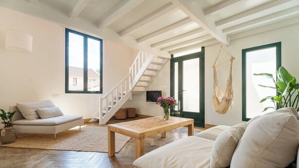 A spacious living room with a wooden floor, a sofa, a coffee table, and a hanging chair. There is a staircase leading to another level, and large windows providing natural light. - L'Arcachon | Hypercentre - Free Parking (Arcachon)