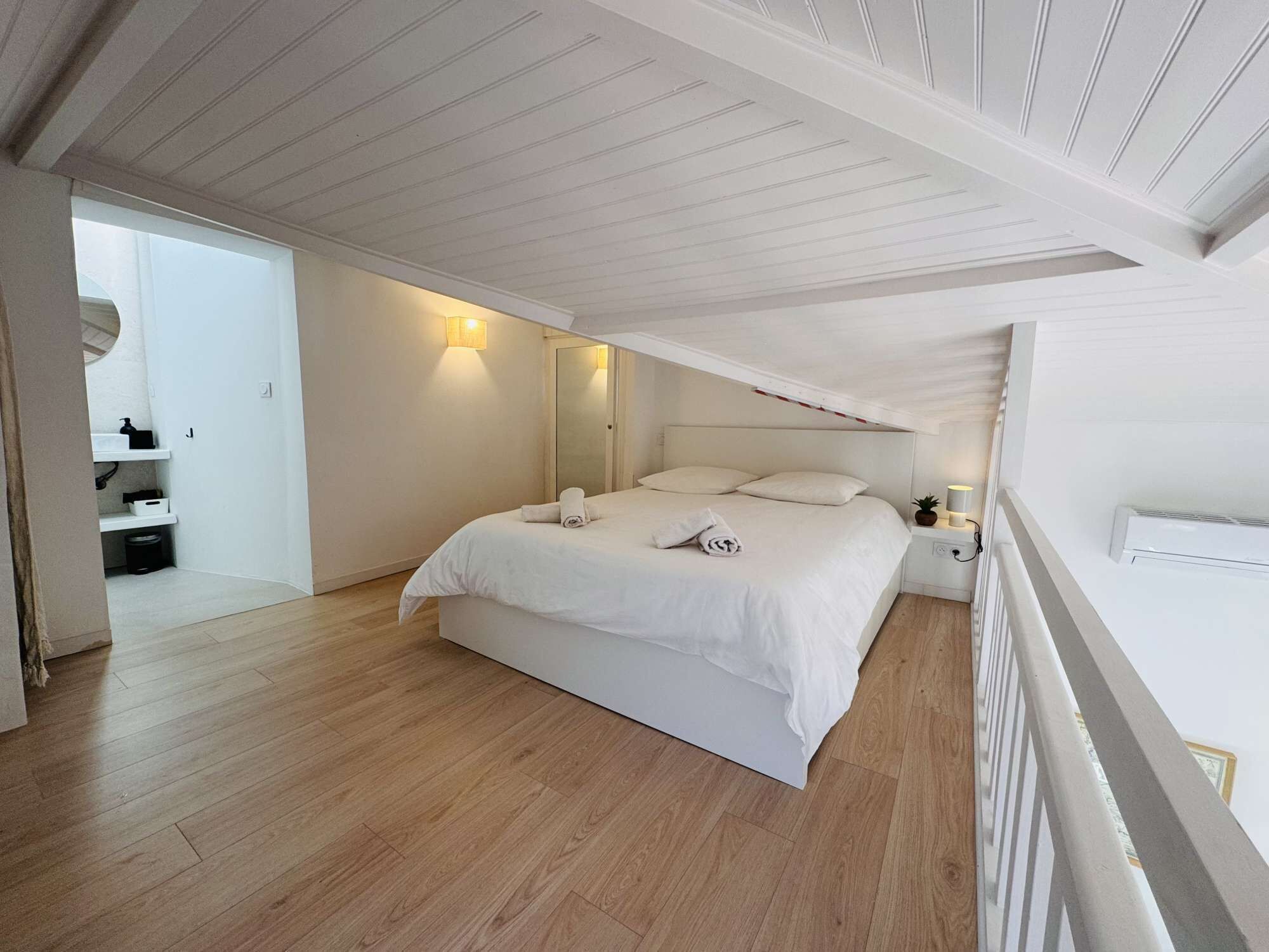 A bedroom with a large bed, white walls, wooden flooring, and a sloped ceiling.