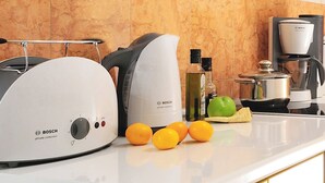 Eine Küche mit Bosch-Geräten, darunter ein Toaster, eine Kaffeemaschine und ein Wasserkocher. Auf der Arbeitsplatte liegen Orangen und ein grüner Apfel.