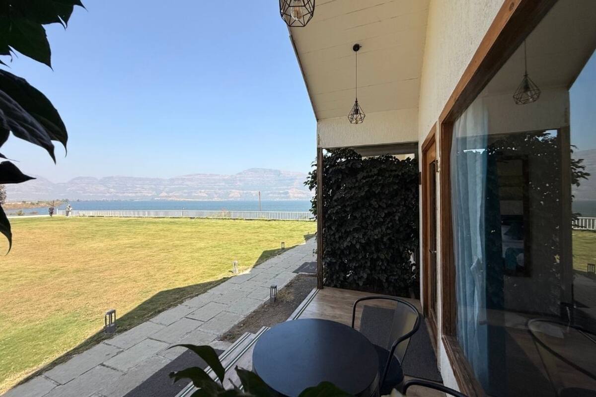 A patio with a table and chairs, a view of a body of water, and a distant mountain range.