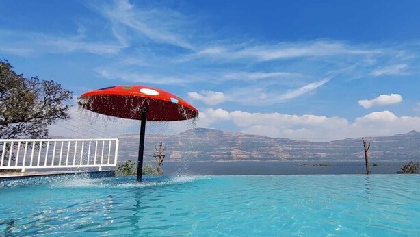 En swimmingpool med ett rött parasoll, vita räcken och en bergig bakgrund.