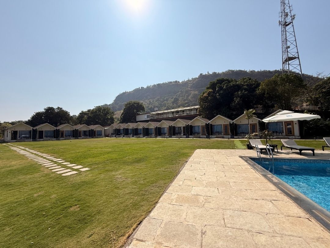 A hotel with a swimming pool, a grassy lawn, and a view of a hill.