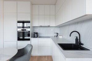 A modern kitchen with white cabinetry, a black sink, and a coffee maker. - Elegant Karlín Apartment with Parking & Terrace by EasyBNB Premium (Prague)