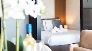 A hotel room with a bed, pillows, a bedside table with a lamp, and a chair. - Mercury Suites (St. Julian's)
