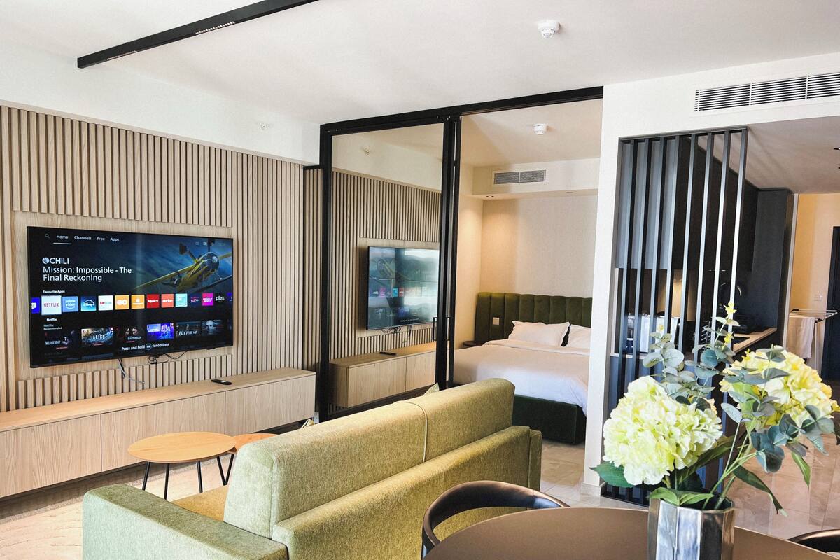 Una habitación de hotel moderna con televisión de pantalla plana, sofá, mesa de comedor y cama.