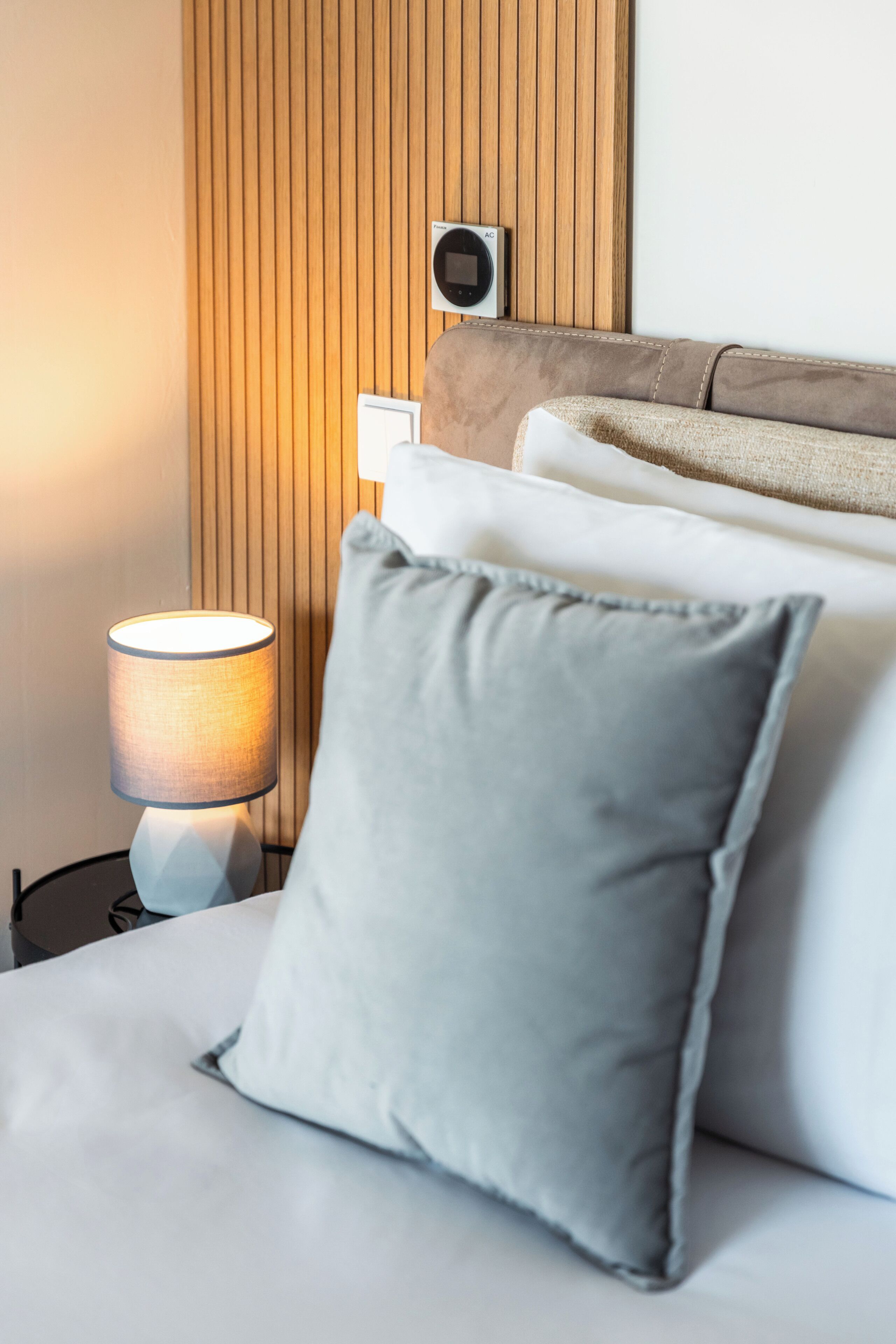 Un lit bien fait, avec un oreiller gris, une lampe de chevet et un climatiseur fixé au mur.