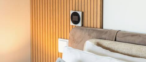 Un lit bien fait, avec un oreiller gris, une lampe de chevet et un climatiseur fixé au mur.