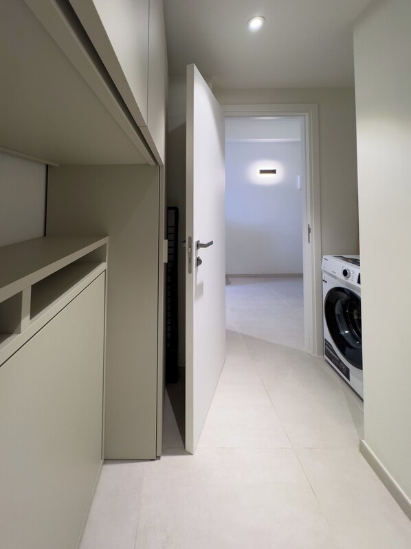 A narrow hallway with a washing machine, a door leading to another room, and a shelf unit. - Mercury Suites (St. Julian's)
