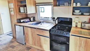 Une cuisine de taille réduite, équipée d’un évier, d’une cuisinière, d’un four et de meubles de rangement en bois.