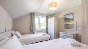 Een slaapkamer met twee bedden, een raam met gordijnen, een kledingkast, een kaptafel met spiegel en een hanglamp.