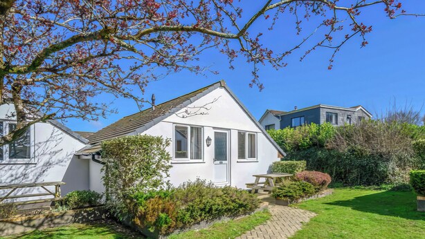 Een witte cottage met een pannendak, een houten bankje en een geplaveid pad naar de ingang.