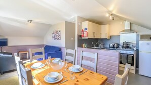 Een eetgedeelte met een houten tafel voor vier personen, een keuken met moderne apparatuur en een gezellige zithoek met een blauwe bank.