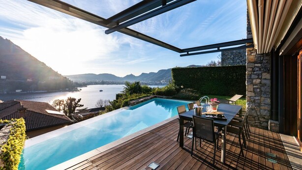 A pool with a wooden deck, outdoor furniture, and a view of a lake and mountains. - Villa Mara - MyHomeinComo (Como)