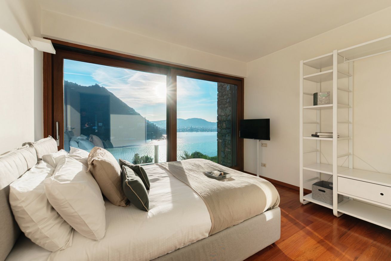 A bedroom with a large bed, a view of a lake, and a white shelving unit.