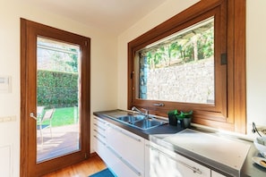 A kitchen with a built-in oven, a sink, and a window overlooking a garden.
