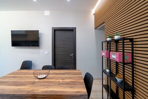 A modern meeting room with a wooden table, black chairs, a TV mounted on the wall, and a wooden slatted wall with potted plants. - Exclusive detached villa with a heated outdoor pool and spa (Sicilia)