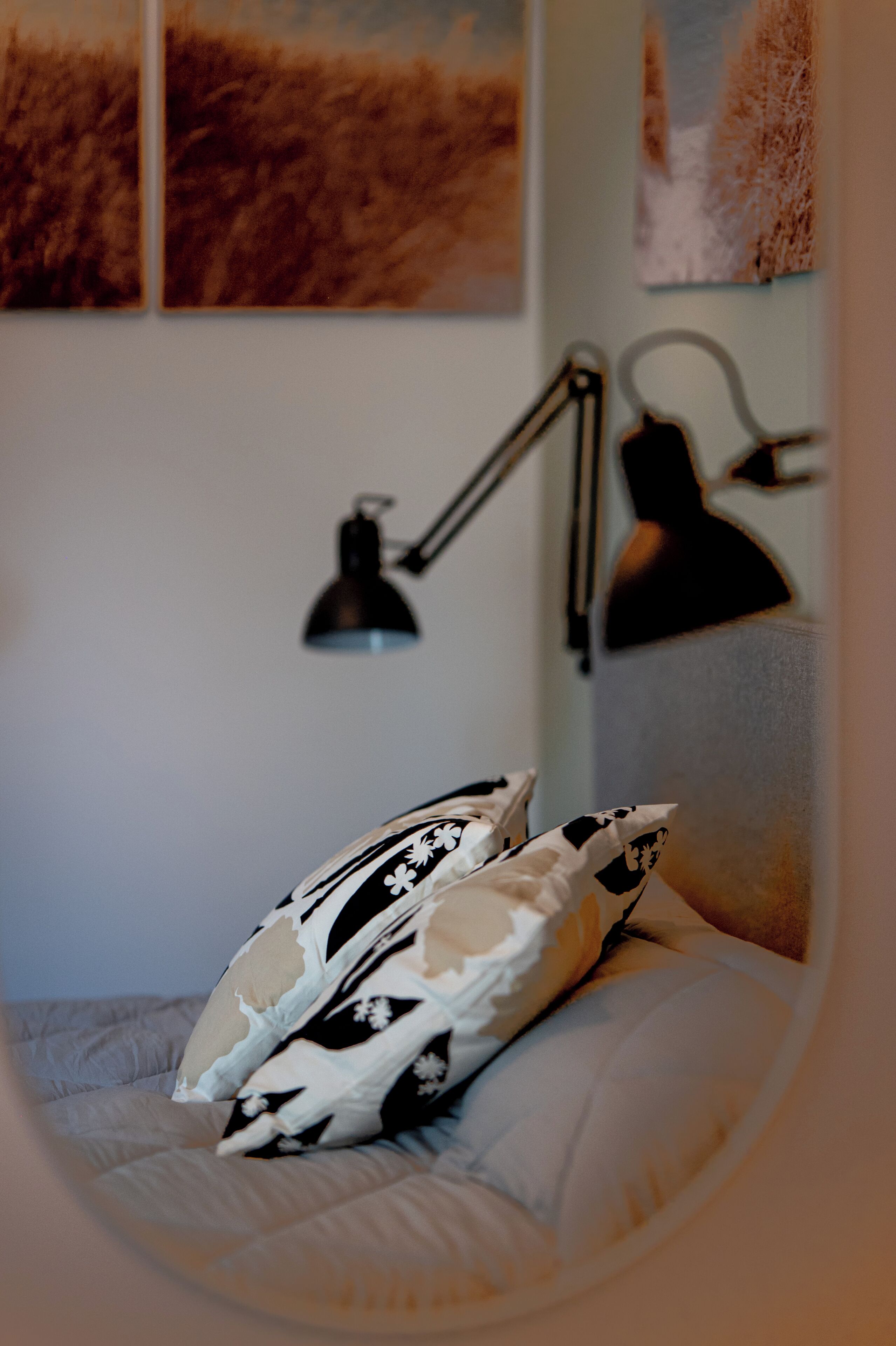 A bed with patterned pillows, a black desk lamp, and framed artwork on the wall.