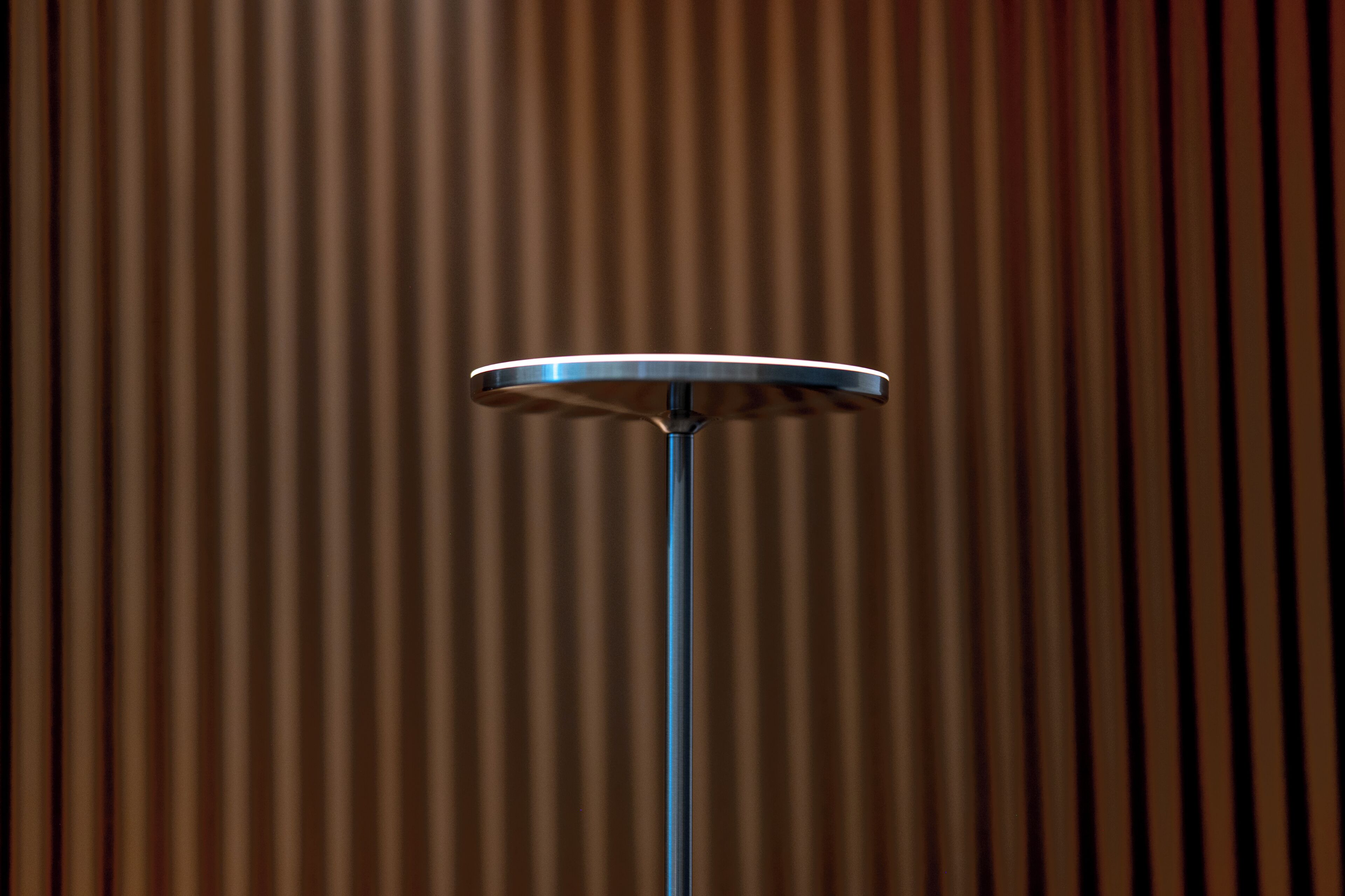 Una mesa redonda con detalles metálicos frente a un fondo de listones de madera verticales.