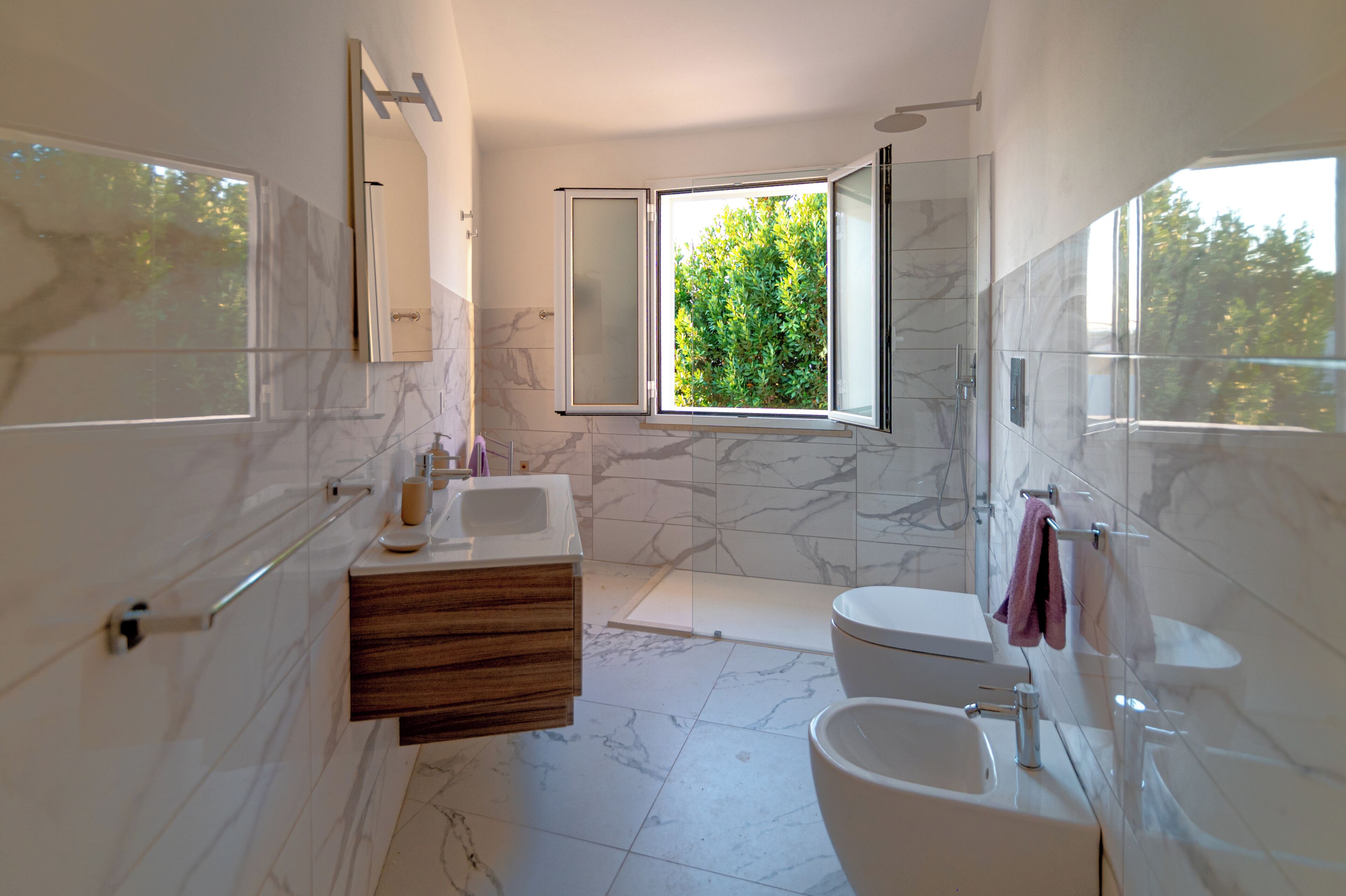 A modern bathroom with a large mirror, a vanity with a marble countertop, a toilet, and a shower area.