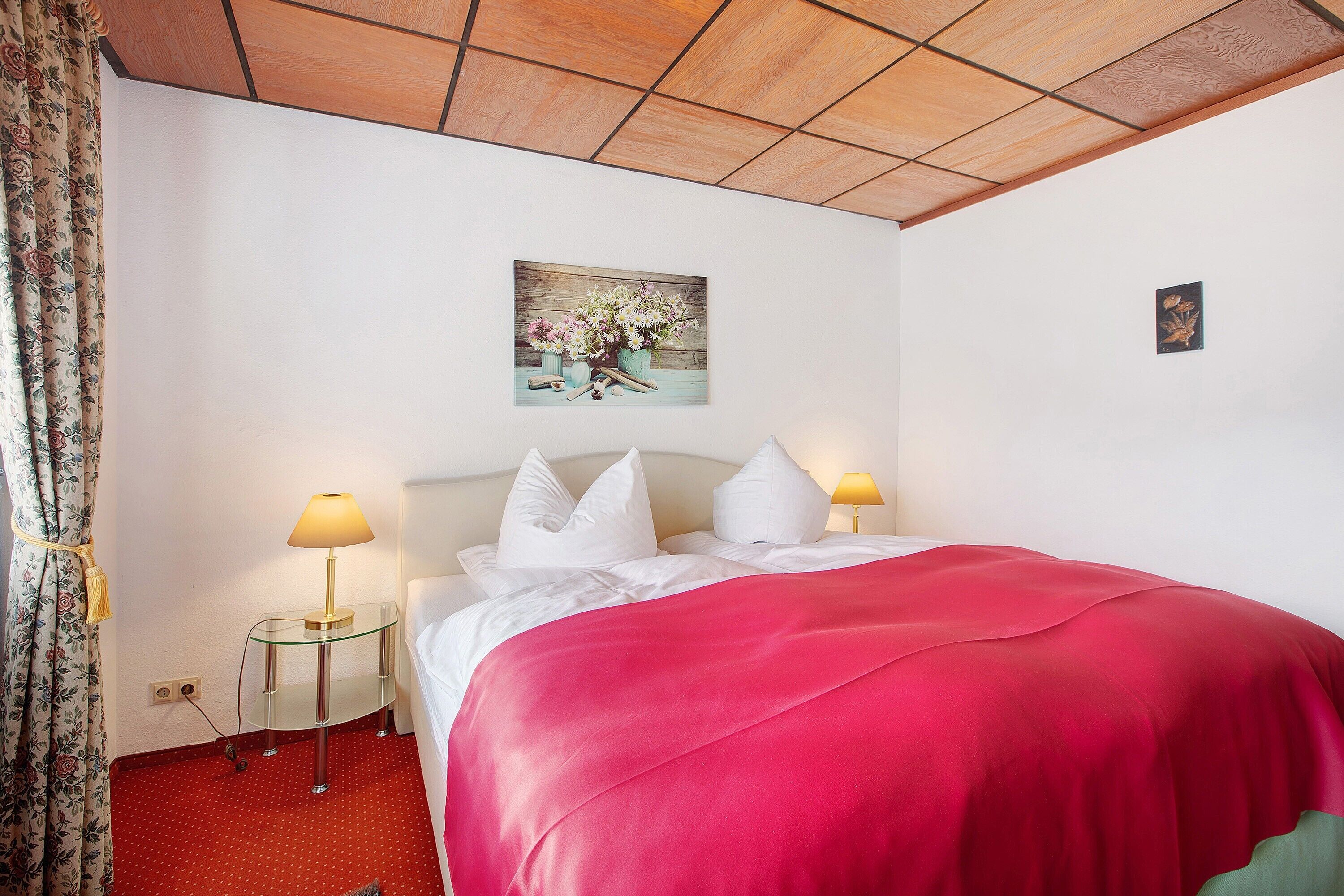 Een hotelkamer met een bed, twee bedlampen, een bloemwerk op de muur en een rood tapijt.