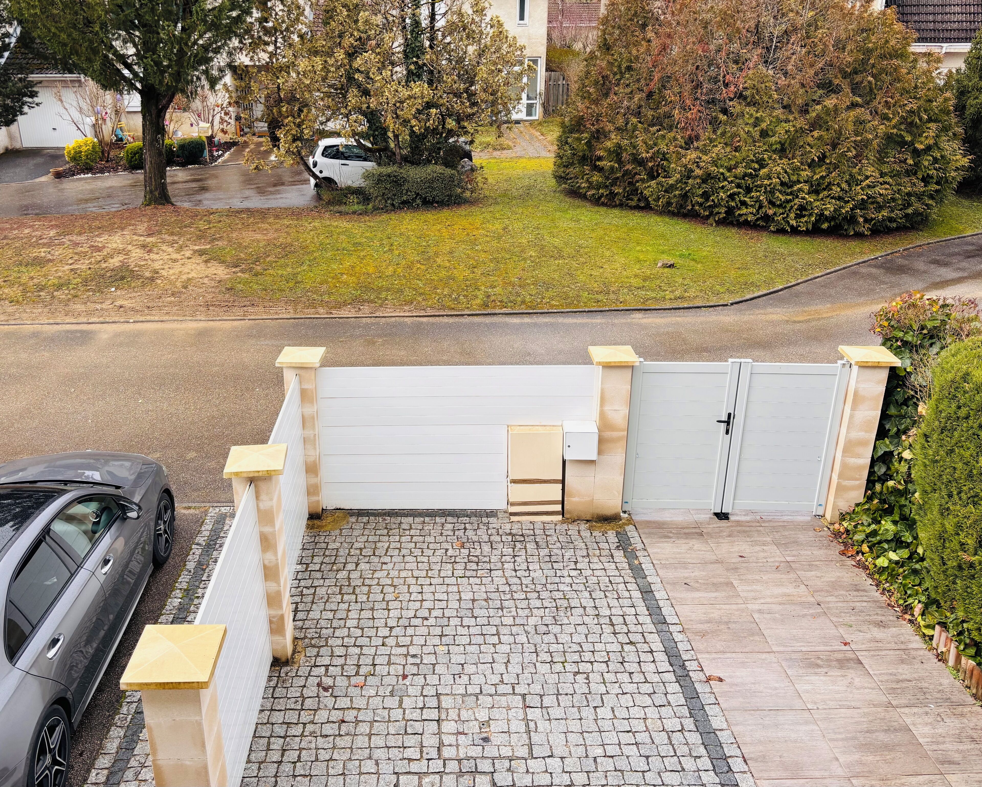A gated driveway with a paved path leading to a white gate.