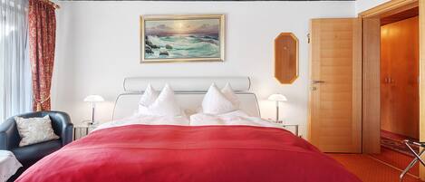 A hotel room with a large bed, a desk, a chair, a painting on the wall, and a wooden door.