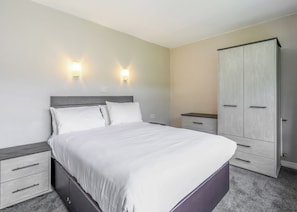 A bedroom with a bed, two bedside tables, a wardrobe, and wall-mounted lights. - Surf Wave Apartment 2 (Pets Welcome) (Woolacombe)