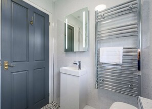 A bathroom with a door, a sink, a mirror, and a towel rack. - Surf Wave Apartment 2 (Pets Welcome) (Woolacombe)