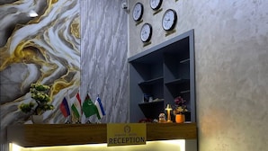 A reception desk with a marble wall, clocks, and flags. - Sumaya Hotel (Tashkent)
