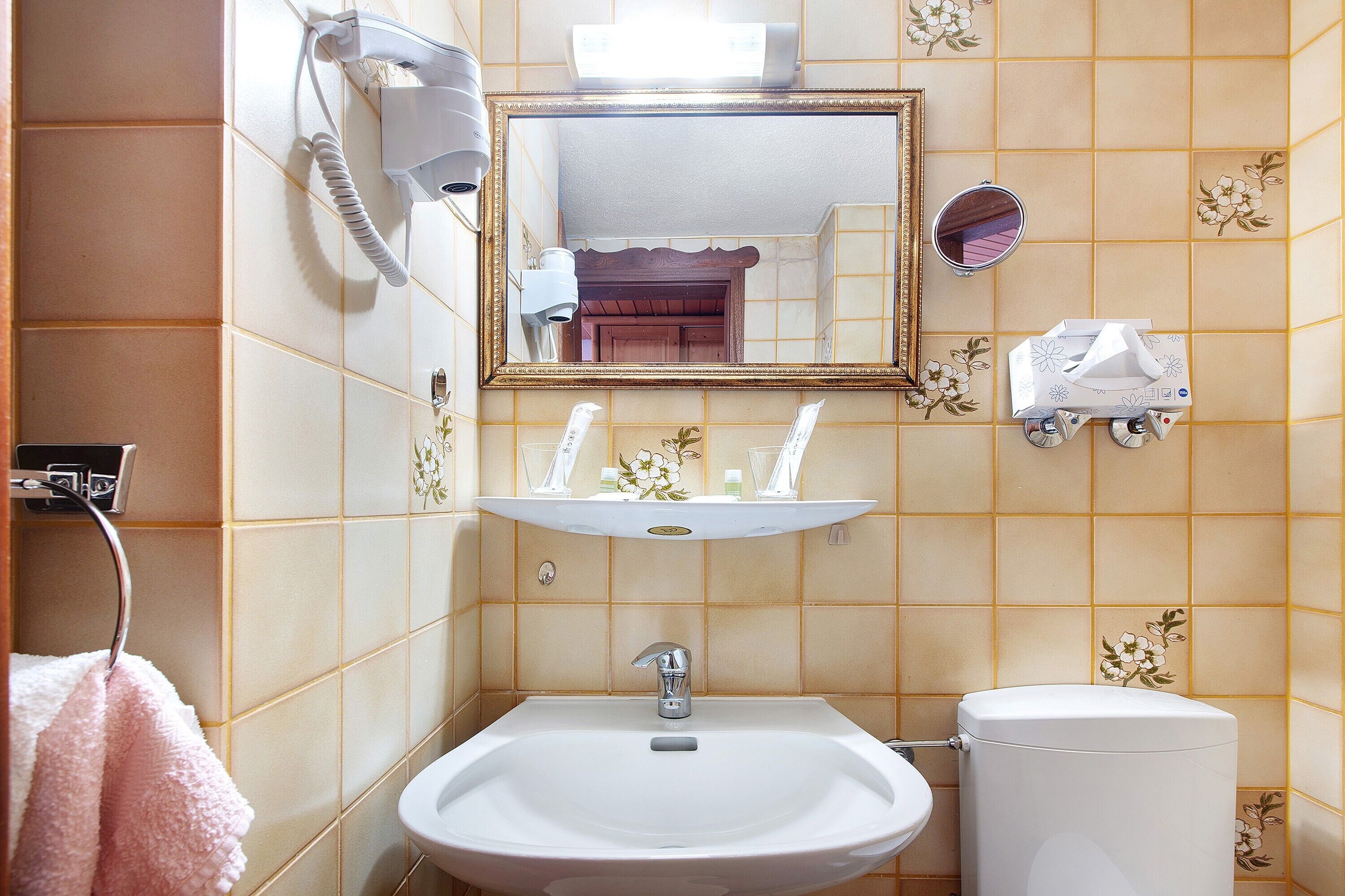 A bathroom with a sink, mirror, toilet, and a hairdryer on the wall.