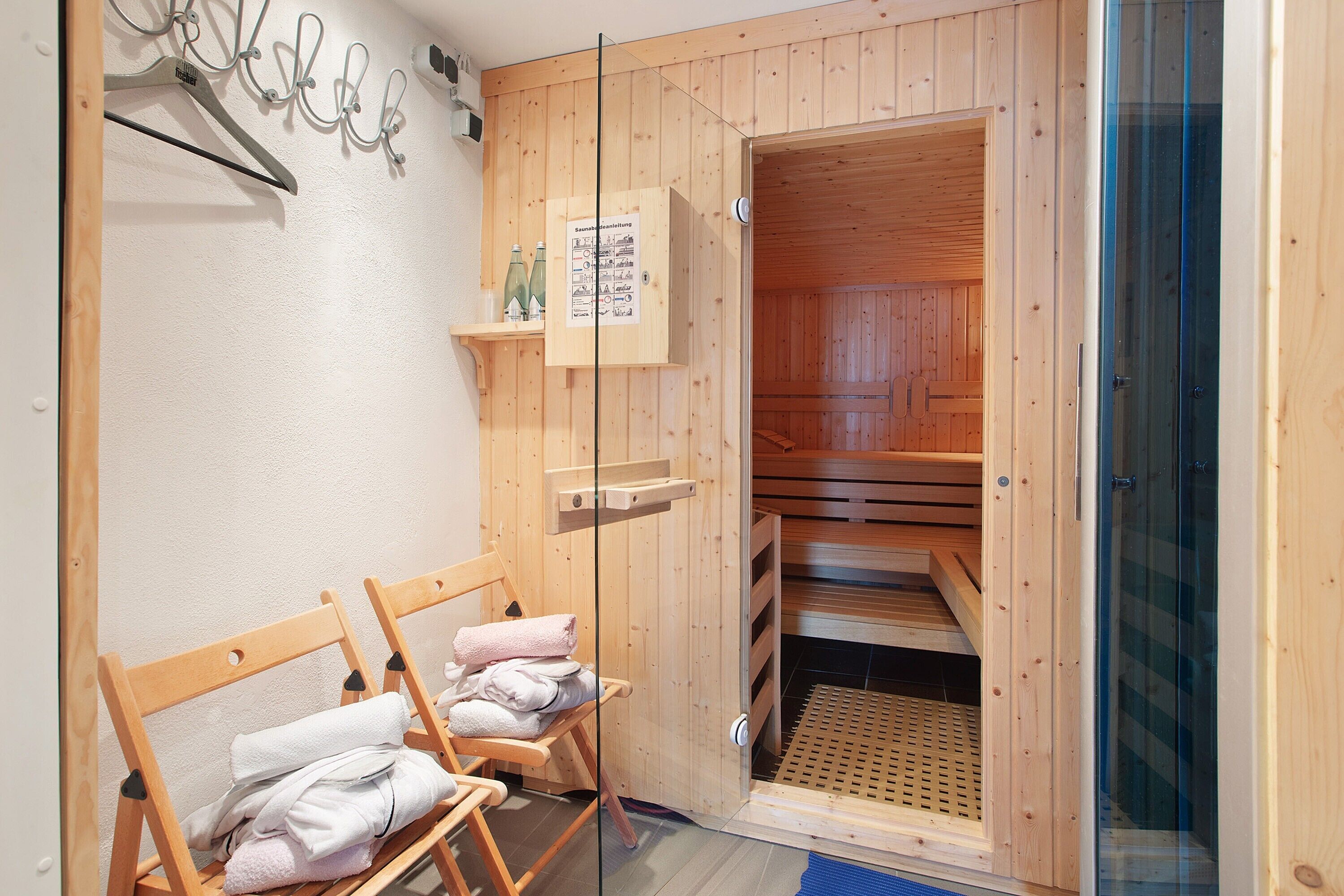A wooden sauna room with benches, towels, and a glass door.