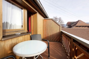 A balcony with a table and chairs, a window with curtains, and a view of a neighboring building.