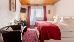 Hotellihuone, jossa on sänky, työpöytä, tuoli, televisio ja ikkuna, jossa on verhot.