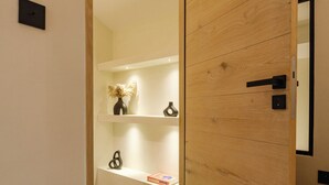 Moderni hotellihuone, jossa on puinen ovi, sänky, yöpöytä ja hylly, jossa on koriste-esineitä.