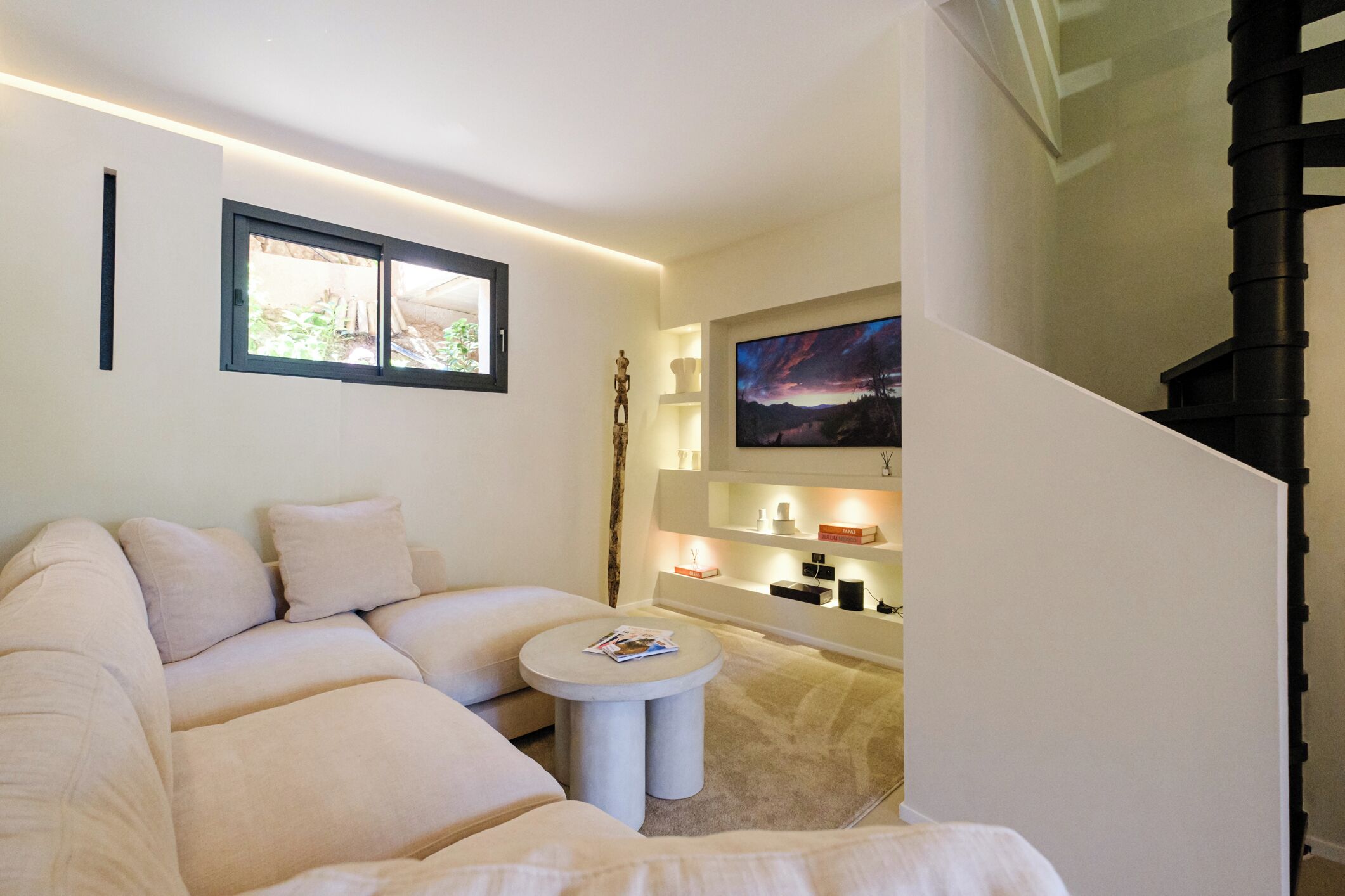 Una sala de estar moderna con un sofá color beige, una mesa de centro redonda, una chimenea y una escalera.