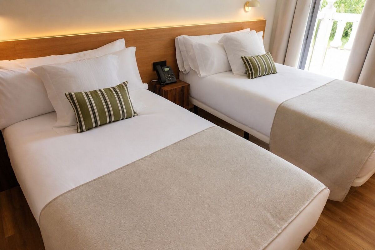Two twin beds with white linens, a bedside phone, and a wall-mounted light fixture.