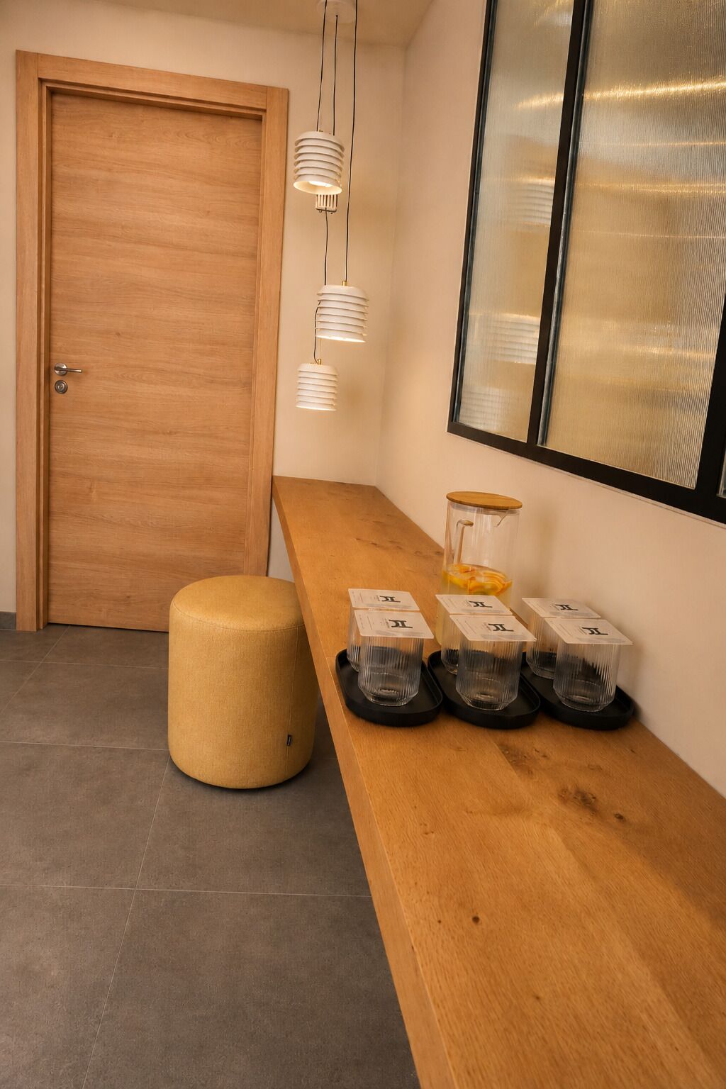 A wooden bench with storage bins, a round ottoman, and a door with a window.